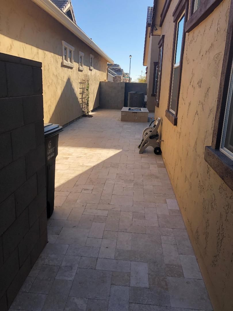 Narrow paved walkway between two buildings with tan stucco walls and a trash can.