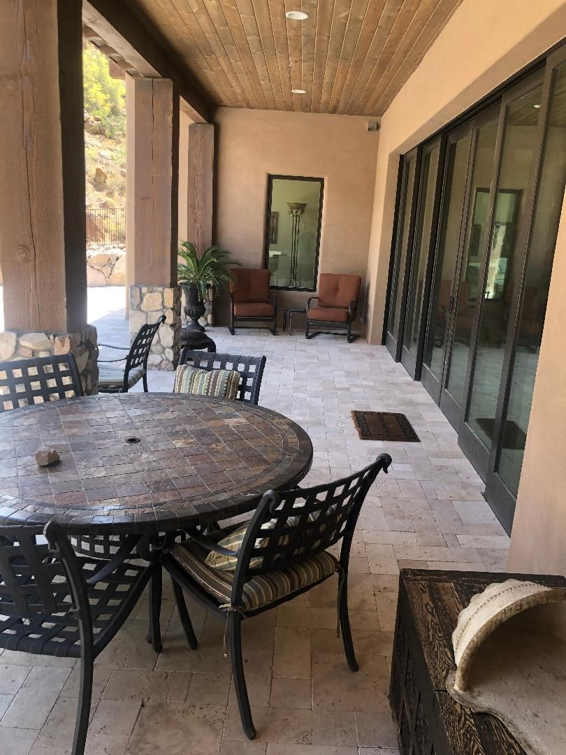 Outdoor patio with a round table and chairs, near a sliding glass door and two armchairs.