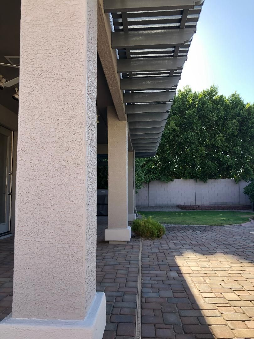 Exterior view of a patio with textured columns, wooden pergola, and brick paving, leading to a grassy yard.