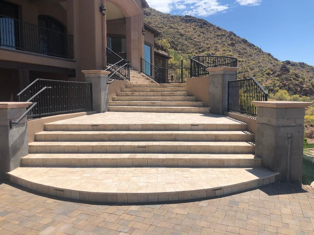 Stone steps leading to a house with black railings. Mountain in the background. Sunny day.