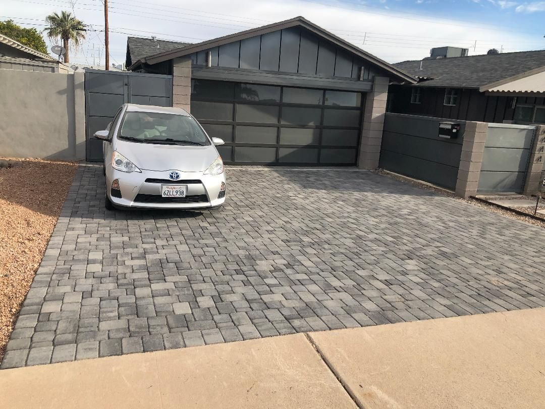 Silver car parked on a gray brick driveway in front of a modern house with a gray garage door.