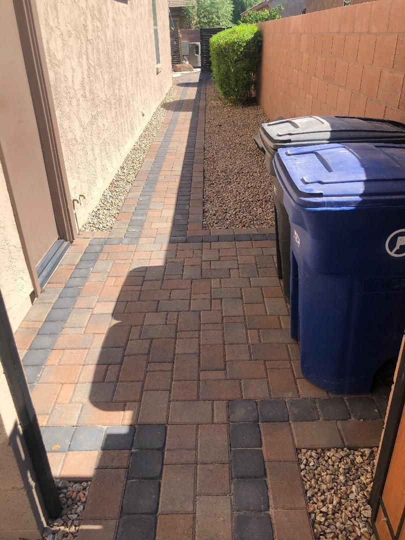 Brick pathway along a wall, with trash cans and landscaping.