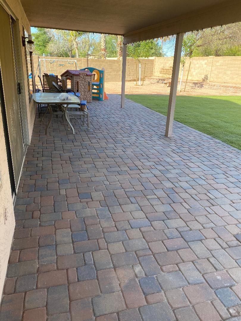 Patio with brick pavers, covered by a roof.  Outdoor setting with grass and play equipment visible.