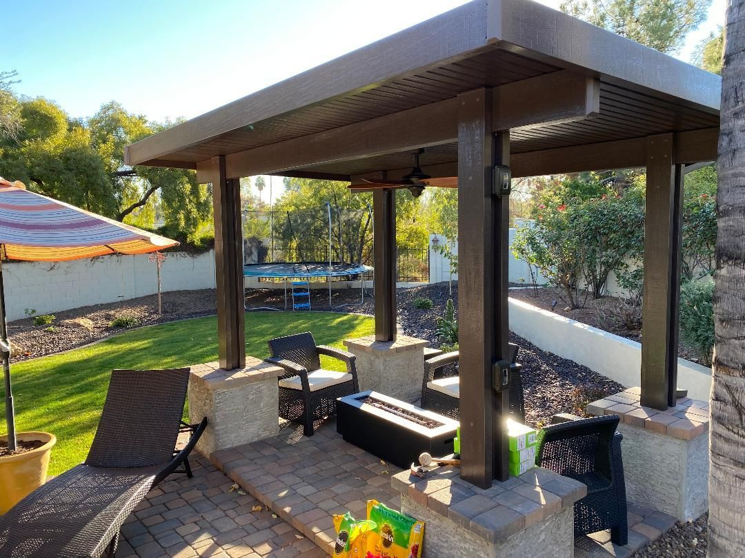 Patio with brown pergola over seating area, fire pit, and lawn in backyard.