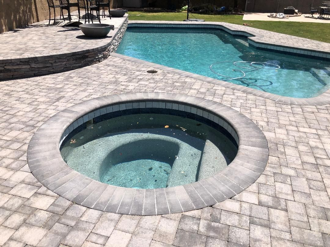 Outdoor backyard with a pool and a hot tub surrounded by grey pavers.