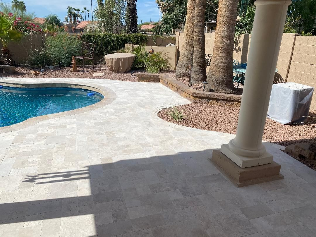 Poolside patio with travertine pavers, pool on the left, and a decorative column on the right.
