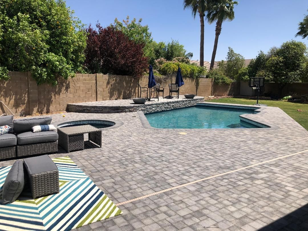Backyard with pool, patio furniture, and landscaping under a sunny sky.