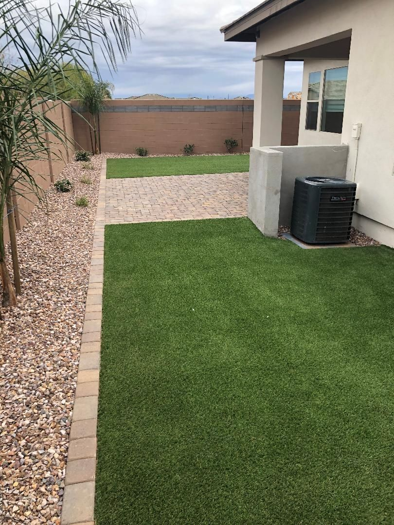 Backyard with green artificial turf, rock border, and concrete wall.