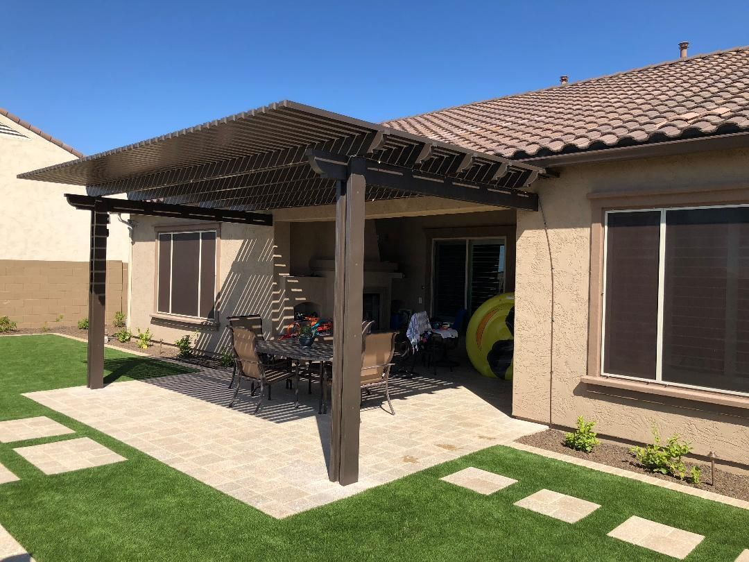 Brown pergola over patio with outdoor seating, adjacent to a home with a tile roof and green lawn.