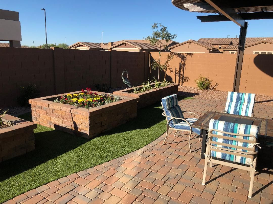 Backyard patio with brick pavers, raised flower beds, and outdoor seating. Brown wall in the background.