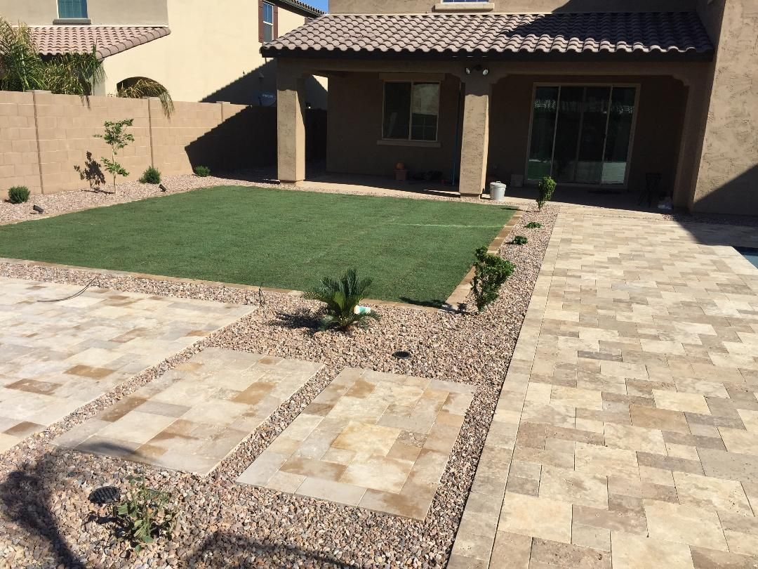 Backyard patio with pavers, gravel, artificial grass, and a covered patio attached to a beige house.