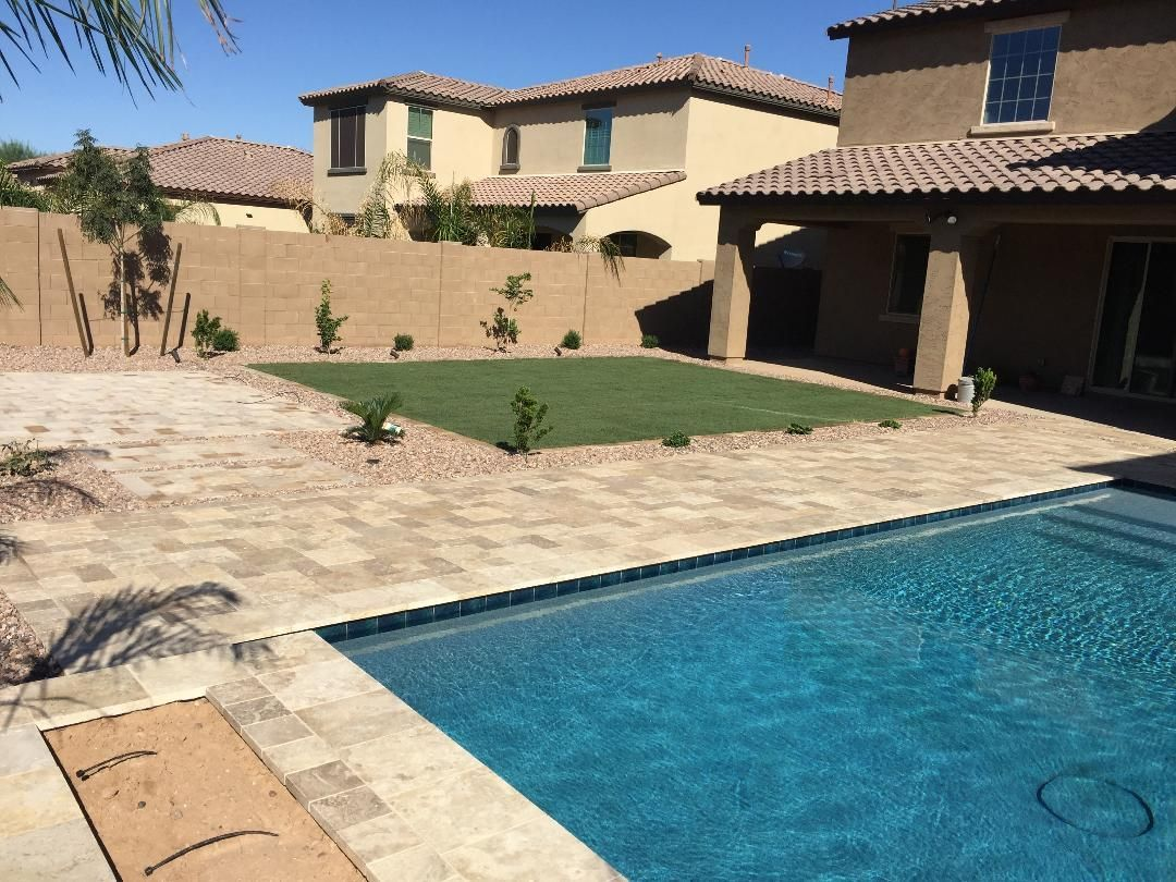 Backyard with pool, patio, small lawn, and tan stucco homes under a blue sky.
