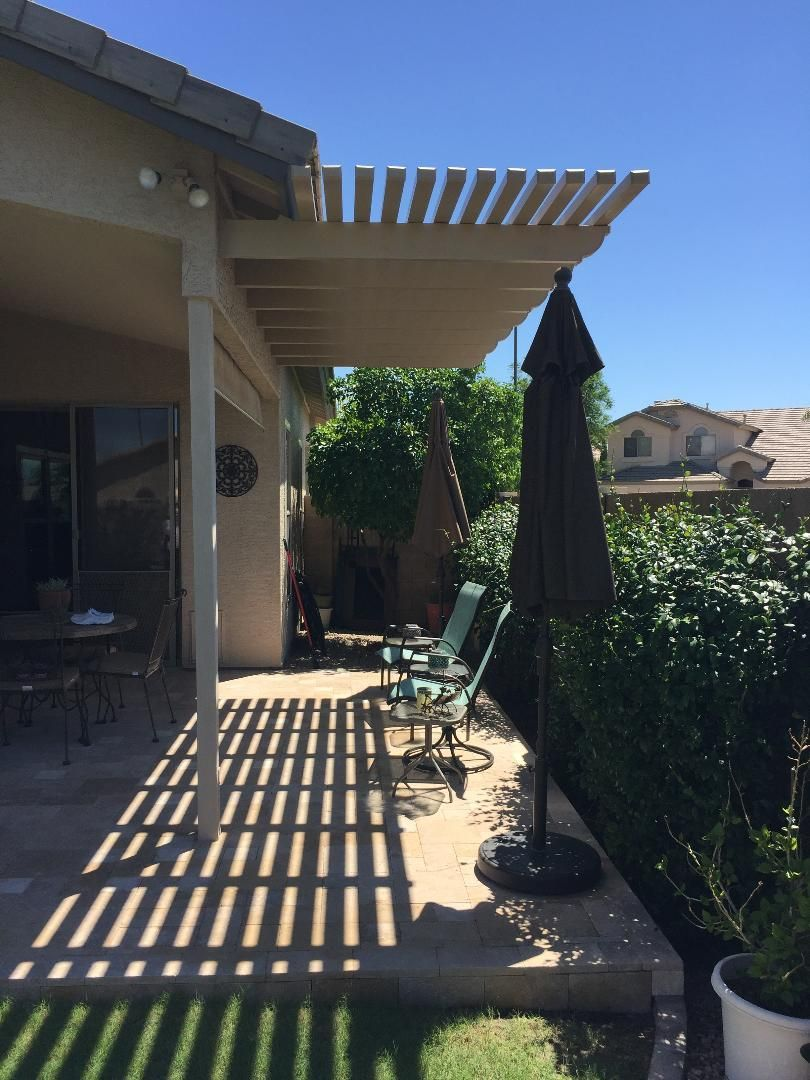 Patio with overhead slats casting shadows; umbrella and chair visible, sunny day.