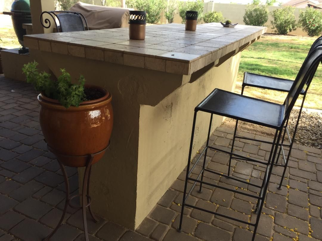 Outdoor bar with tile countertop, bar stools, potted plant.
