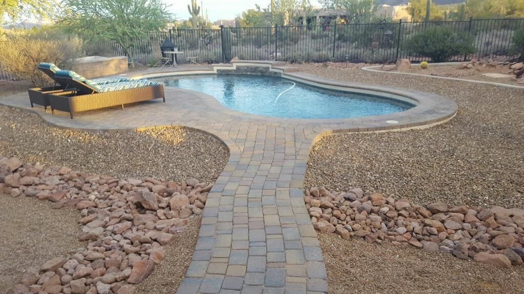 A backyard with a kidney-shaped pool, a brick pathway, lounge chairs, and desert landscaping.