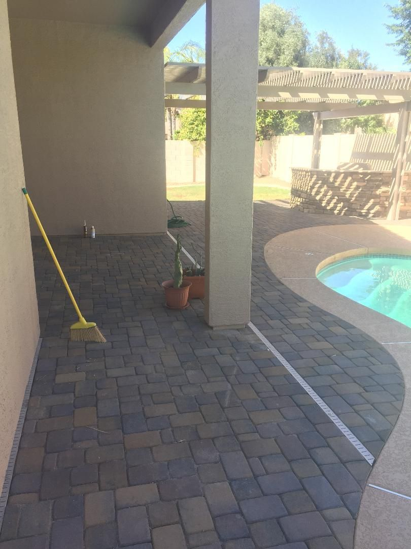 Patio with brick pavers, column, pool, and a pergola in the background.