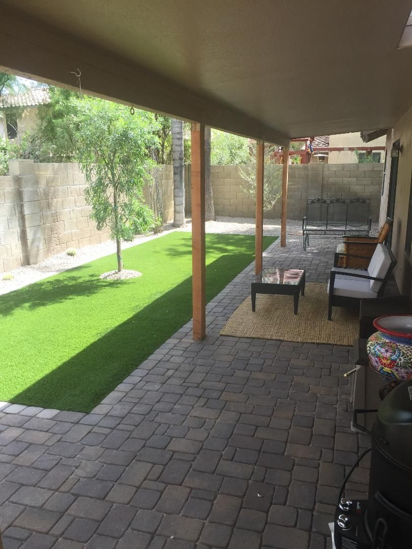 Covered patio with brick pavers, artificial grass, wooden posts, and outdoor furniture.