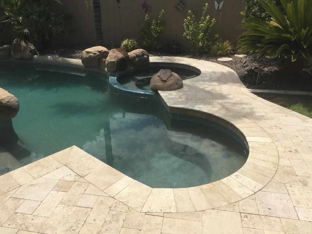 Pool and jacuzzi with waterfall feature surrounded by light-colored paving stones.