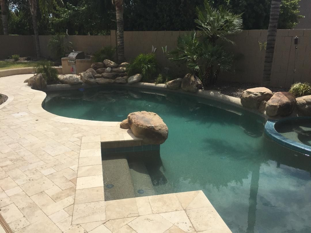 Pool with stone pavers and landscaping. A large rock sits in the center of the pool with blue-green water.