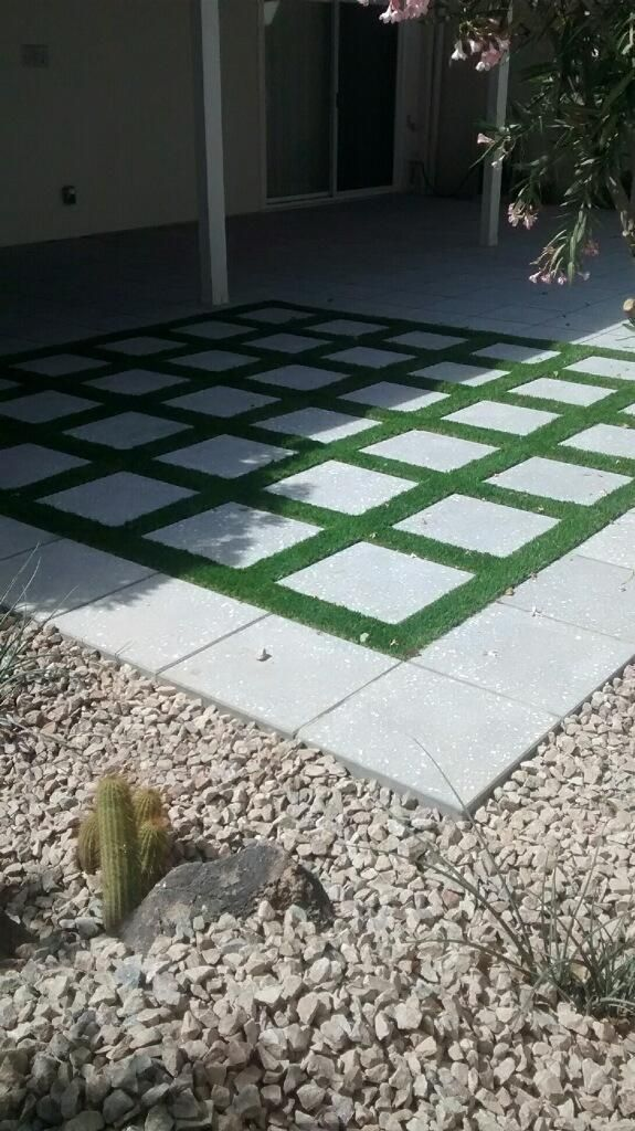 Patio with square pavers and green turf grid, bordered by gravel landscaping and a cactus.