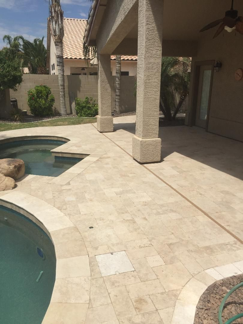 Patio with pool, beige stone, covered area with columns. Blue pool water. Bright sunlight.