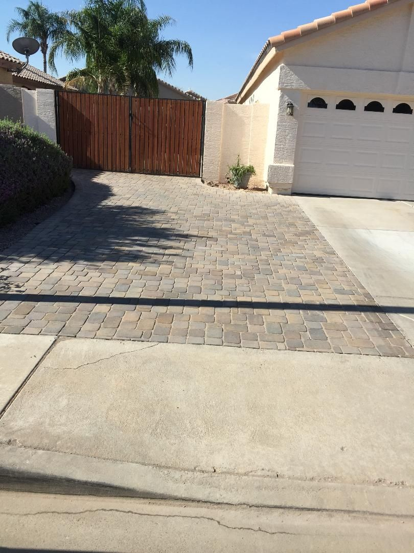 Driveway with brick pavers and a wooden gate leading to a house with a garage.