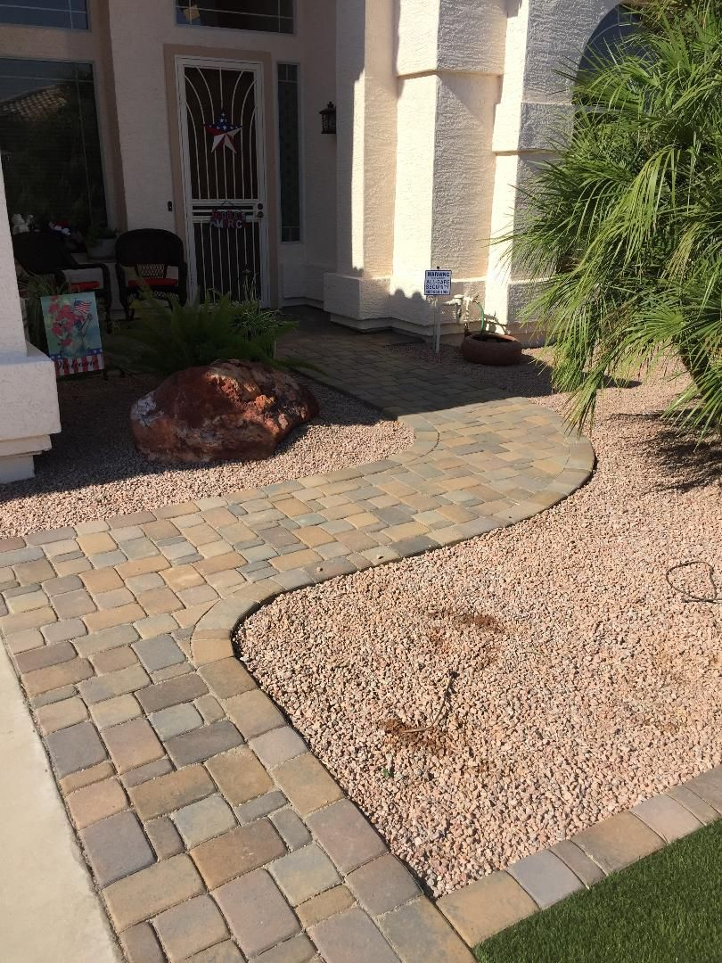 Paver walkway curving to a house entrance, with rock landscaping.