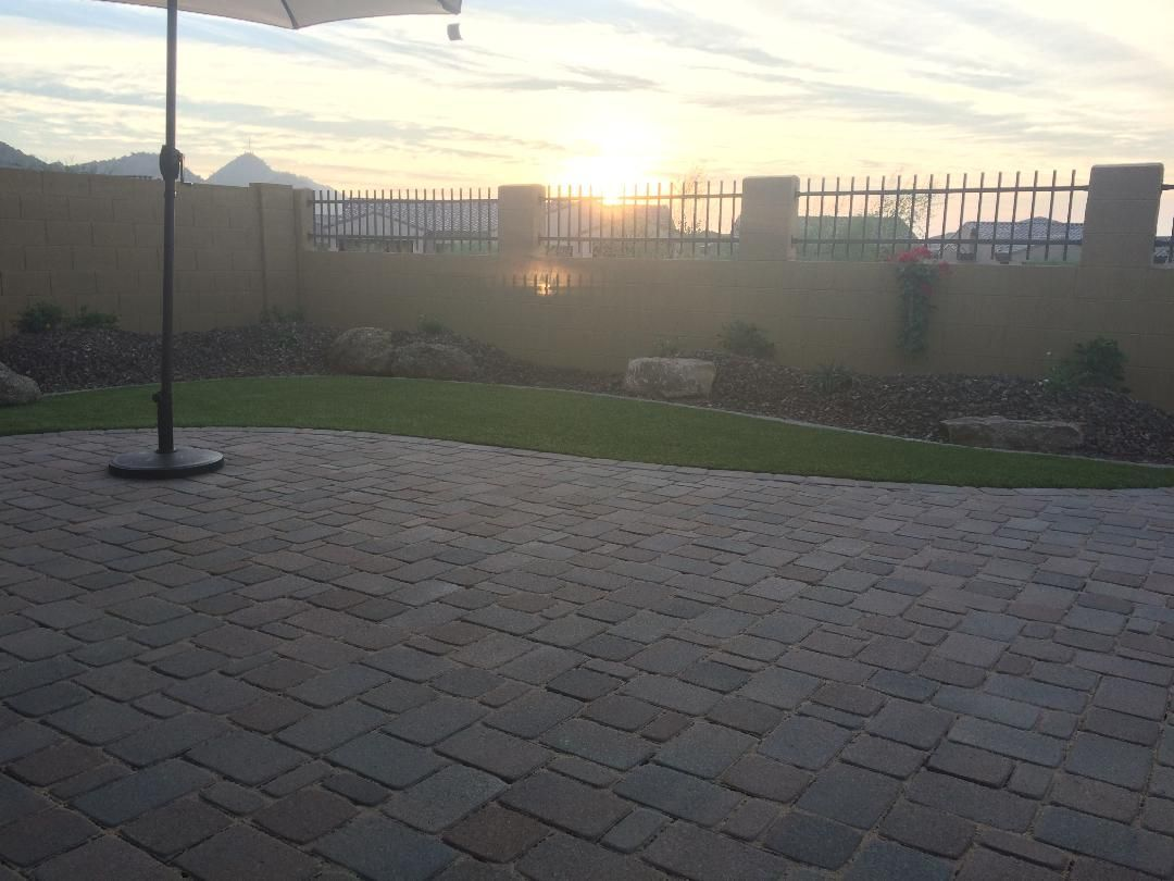 Patio with brick pavers, small lawn, wall with fence, and sunset in the background.