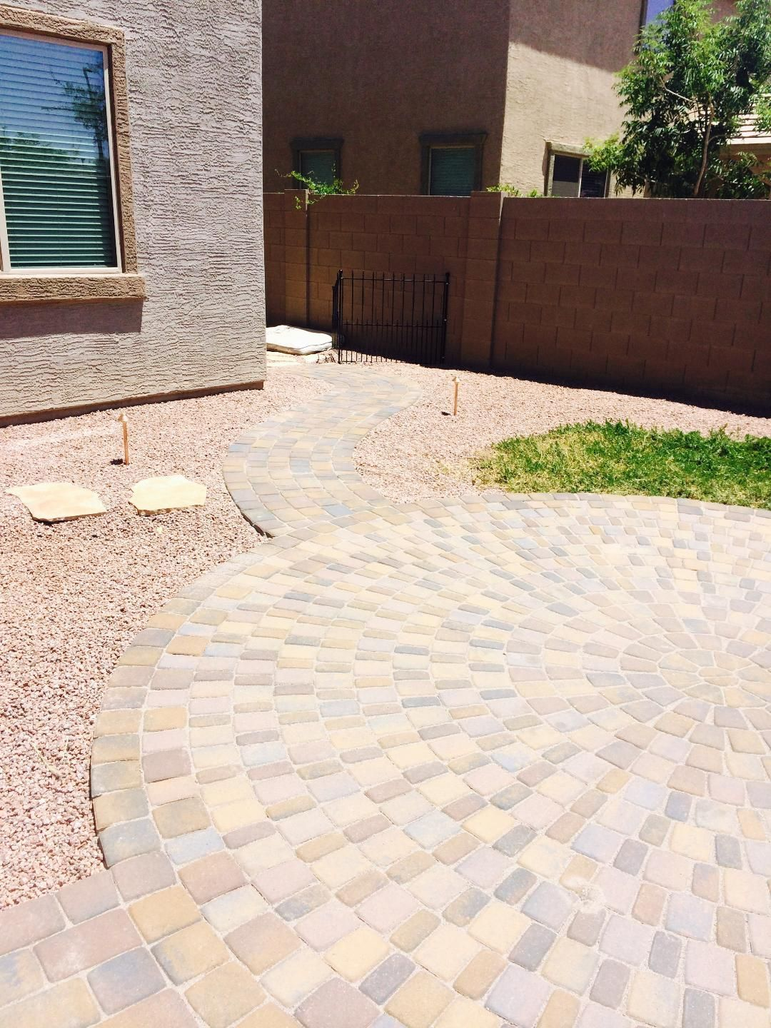 Circular brick patio with gravel path, leading to small grass patch and wall.