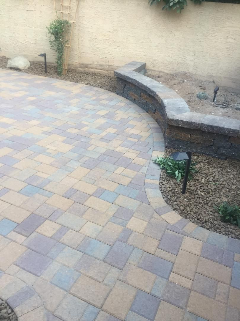 Brick patio with curved border, low stone wall, and desert landscaping.