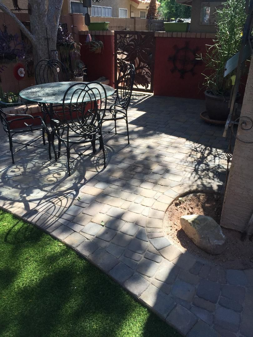 Patio with table and chairs, brick pavers, red wall, decorative metal gate, and green lawn.