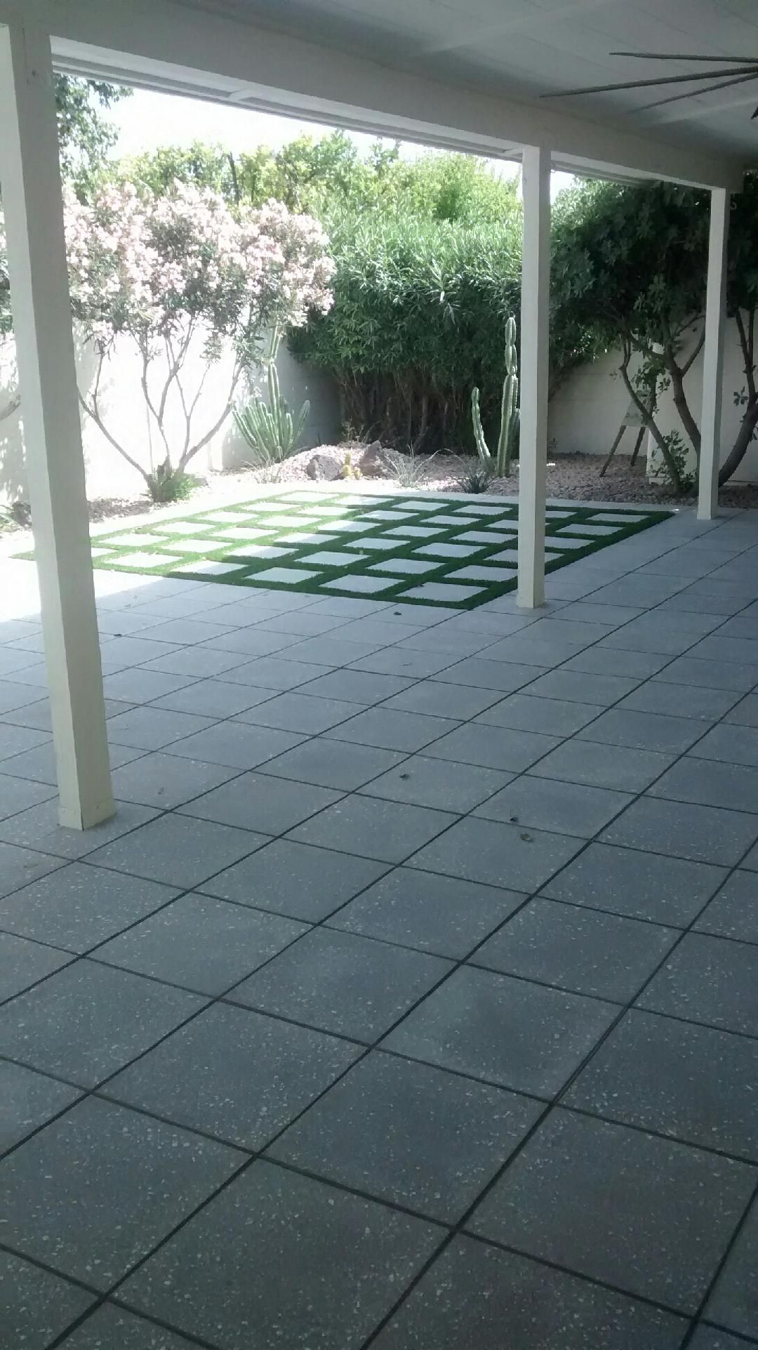 Patio with tiled floor and artificial grass squares, leading to a garden with trees.