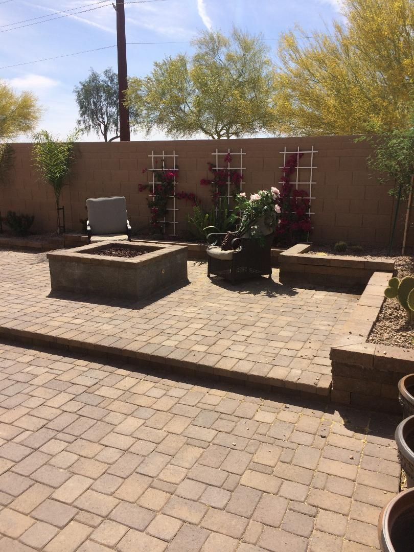 Brick patio with fire pit, planters, and climbing plants against a wall. Sunny day, desert landscaping.