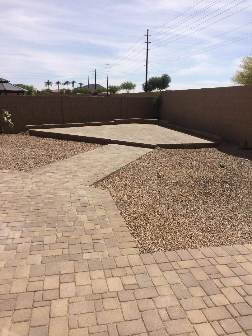 Backyard with brick path, gravel, and a patio against a brown wall. Power lines visible in the background.