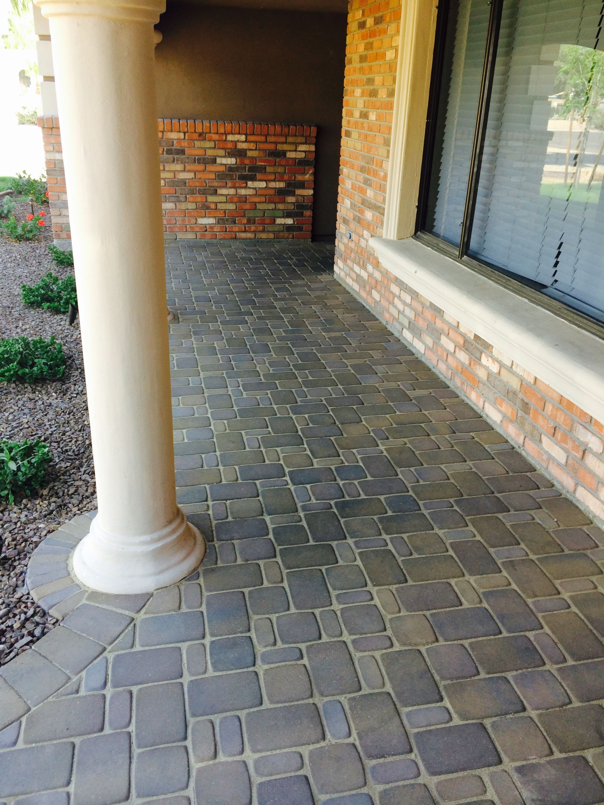 Brick home porch with a patterned paver floor, a white column, and a window.