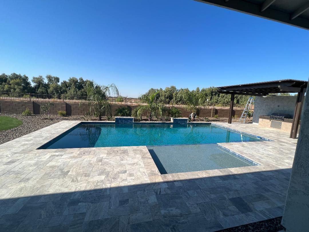 A rectangular swimming pool with turquoise water and a stone patio under a blue sky.