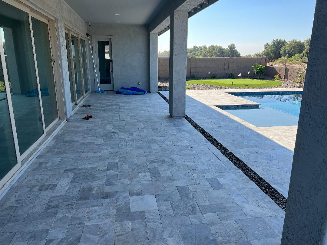 Patio with stone tile flooring, leading to a pool. Sliding glass doors and a covered area are visible.