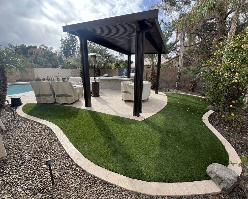 Backyard patio with pergola, seating, fire pit, and a pool. Artificial turf and stone border.