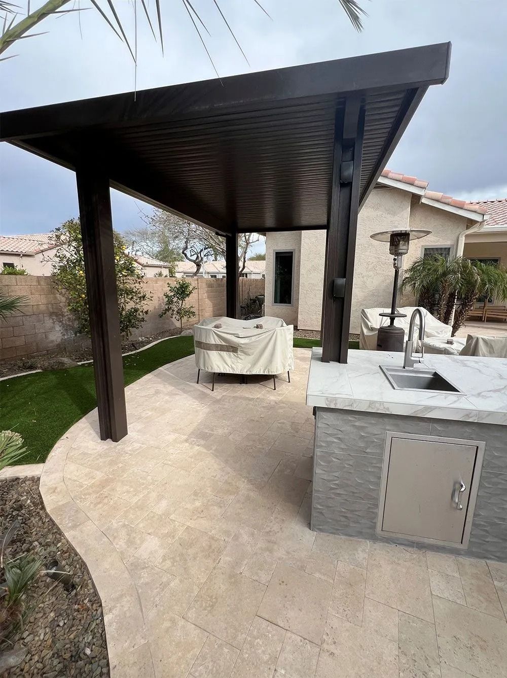 Patio with dark pergola, outdoor kitchen, covered table, and beige flooring.