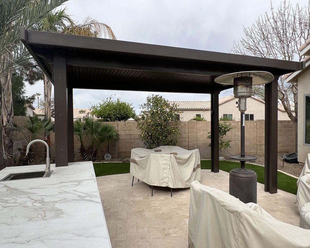 Outdoor patio with dark brown pergola, outdoor kitchen, and covered furniture.