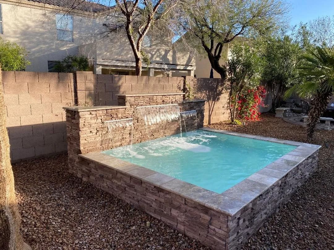 Small outdoor pool with waterfall, surrounded by stone and landscaping.
