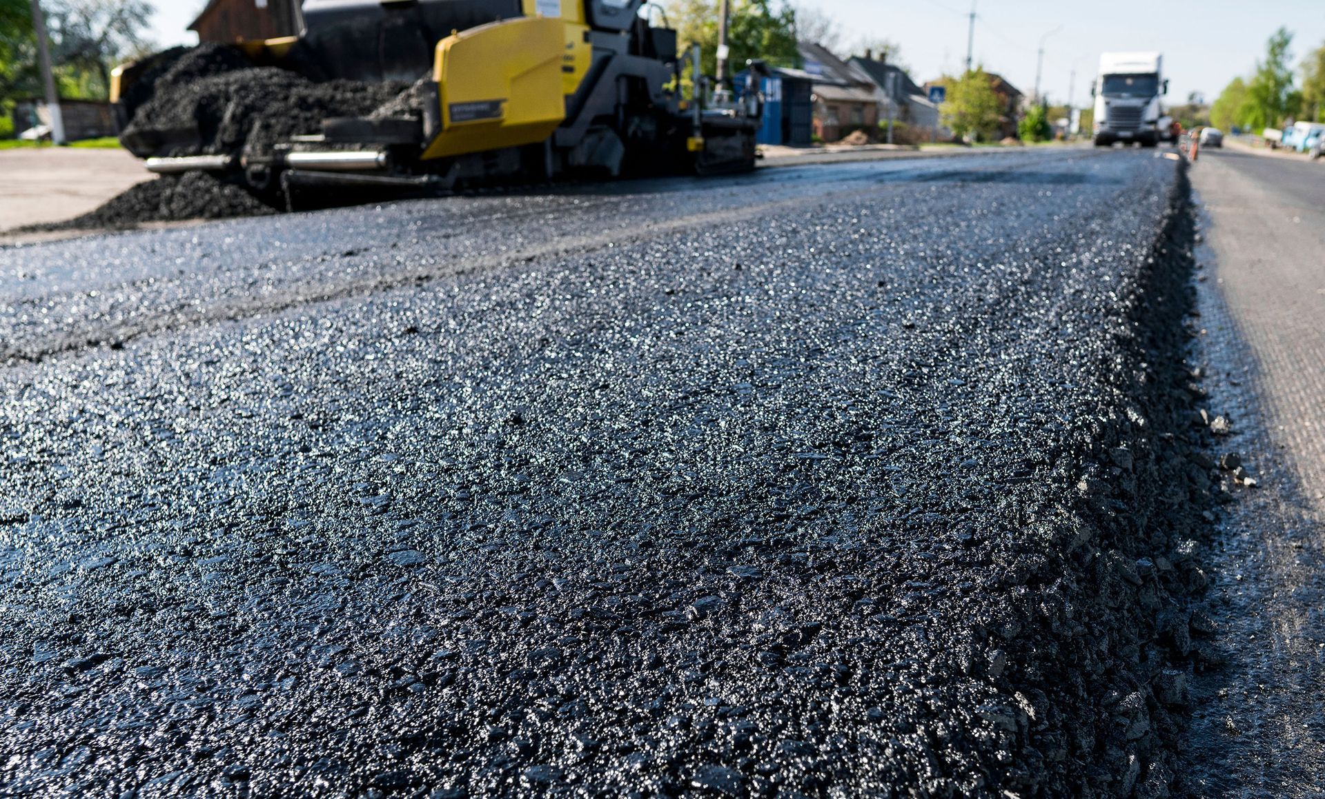 Road paving with asphalt, a yellow paver machine, and a truck on a sunny day.