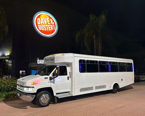A white bus is parked in front of a Dave & buster 's restaurant.