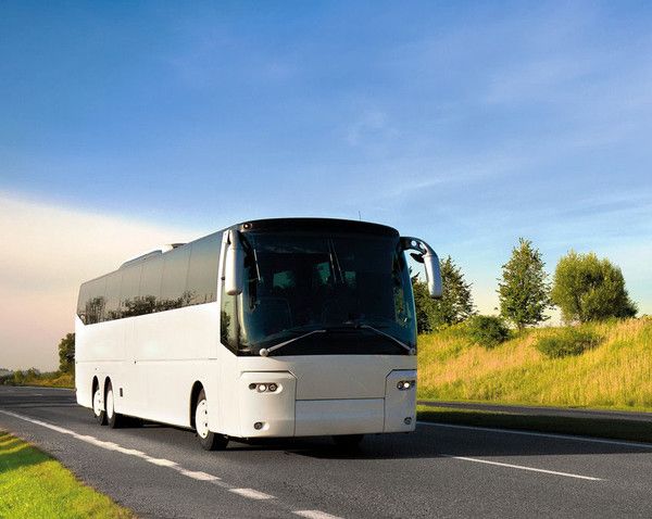 A white bus is driving down a country road.