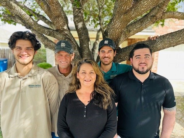 Five people pose under a tree; a woman in black, four men, a house in background.