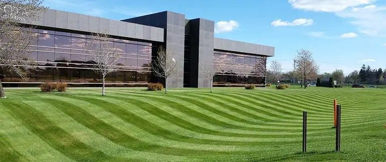 A modern building with reflective windows and a manicured lawn with striped patterns. Blue sky in the background.