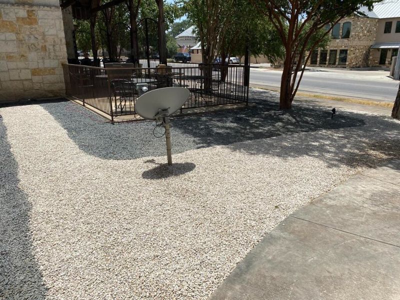 Gravel pathway with satellite dish, near a building and road.