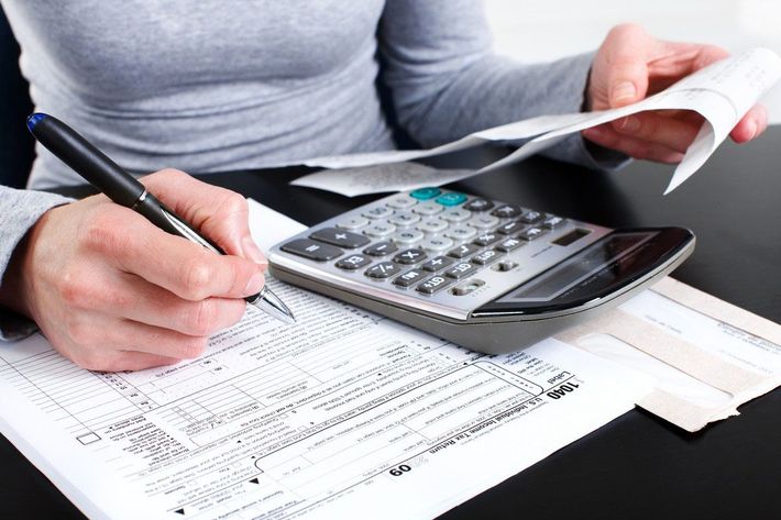 A woman is using a calculator and writing on a piece of paper.