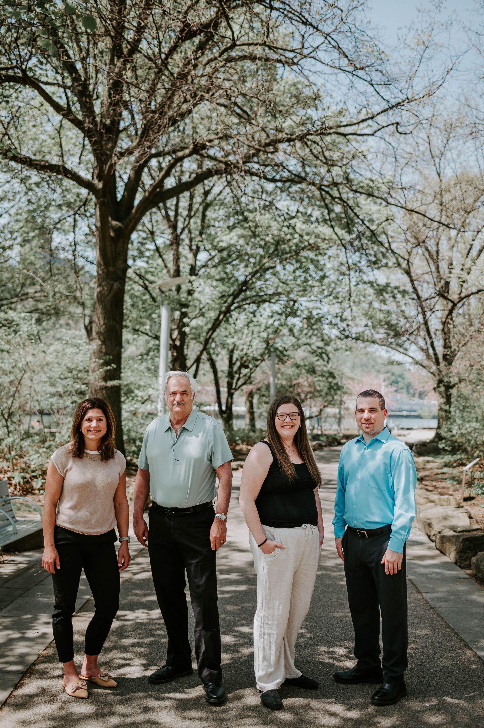 Four people standing outside; two women and two men posing on a path. A large tree is behind them.