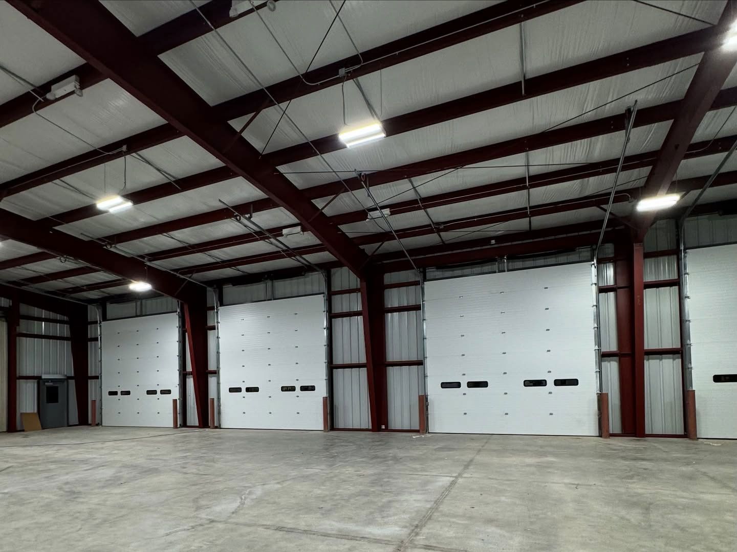 Large empty warehouse with white overhead doors, red steel beams, and concrete floor.